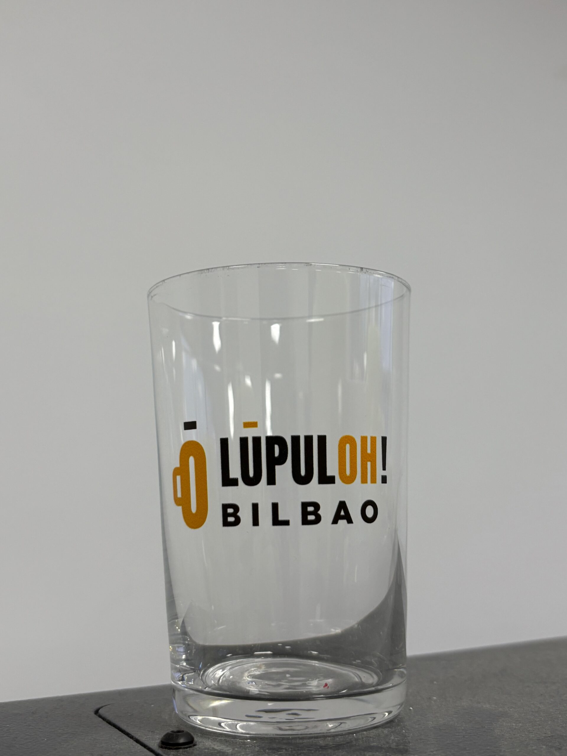 Detalle frontal del logotipo Lúpuloh! Bilbao sobre un vaso transparente